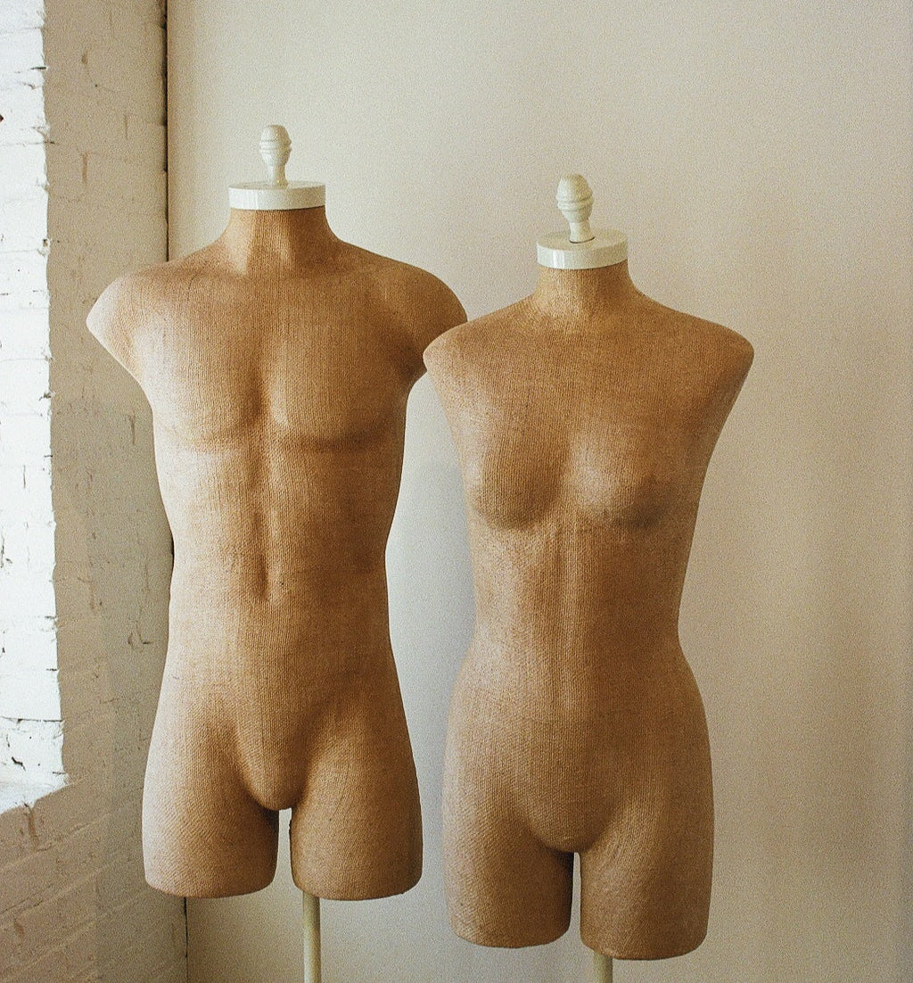 Two beige mannequins on stands against a plain wall.